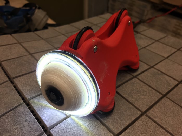 En 3D-printad röd kamerarigg med inbyggd belysning placerad på ett kaklat golv.