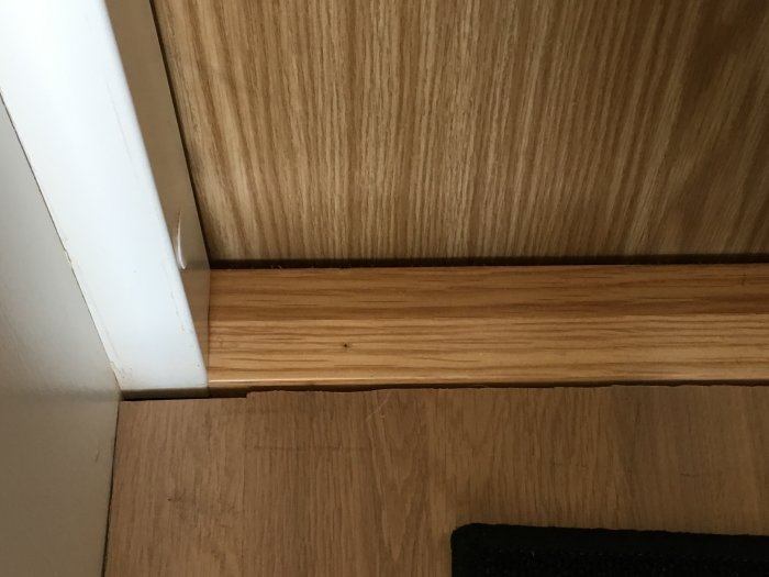 Tröskel med dåligt kapade golvplankor som möter en dörrlist.