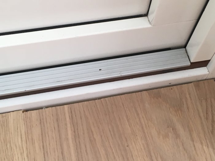 Dåligt anpassat trägolv nära dörrtrösk och golvlister som visar glipor.
