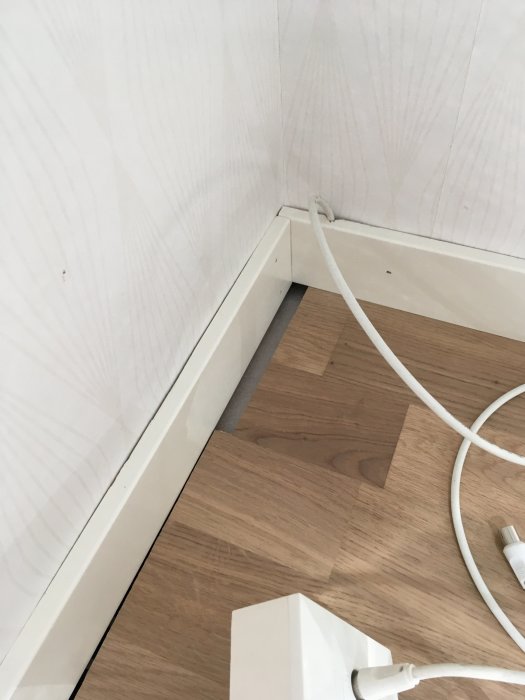 Felaktigt avkapade trägolvplankor intill en vit vägg och golvlister med synliga mellanrum.