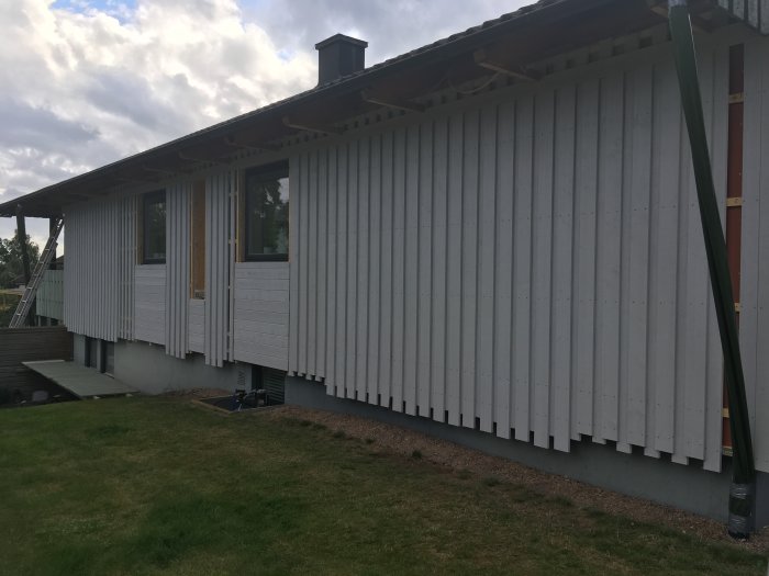 Nypanelat hus med vit träpanel, halvfärdigt byggprojekt med vindskydd och gräs i förgrunden.