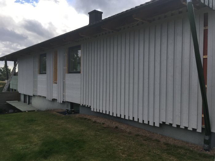 Nybyggd vit vägg på hus med stege och byggmaterial synligt.