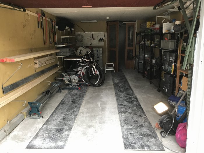 Organiserat garage med verktygstavla, cykel, arbetsbänk och hyllor fulla av förvaringslådor.