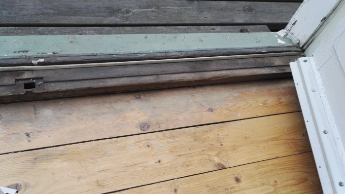 Närbild på en altandörrs tröskel med synlig slitage och tecken på möjlig läckage där dörren möter golvet.