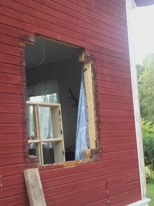 Ett rött hus med ett fönster som saknar ram och kalkbruket runt fönstret ser ut att ha rasat.