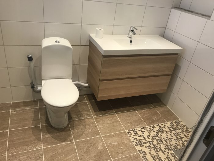 Nyinstallerad vit toastol och beige kommod med handfat i ett kaklat badrum.