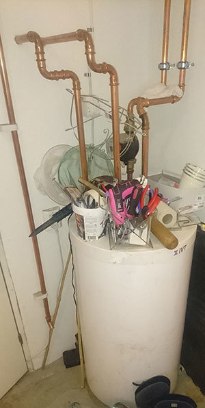 Värmesystem med bergvärmepump och ett kopplat vitt kärl, omgiven av kopparledningar och verktyg.