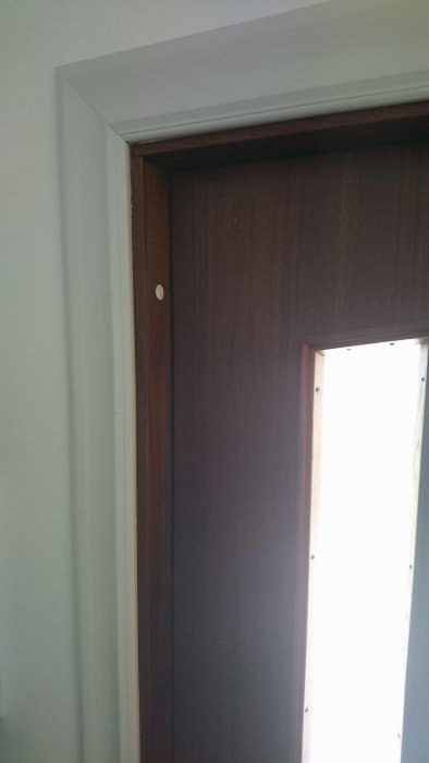 En dörröppning med foder, visar insida av brun dörr och vit dörrkarm.