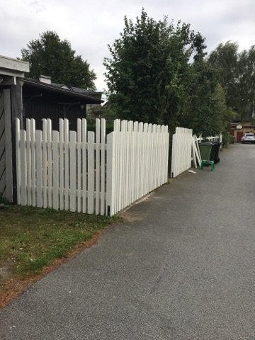 Vitmålat staket med ojämn överkant och en synlig glipa mellan staketdelarna.