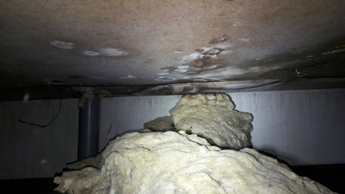 Bild på fuktangrepp och mögelskador underifrån i en krypgrund med synlig rörledning och isolering.
