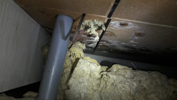 Bild på fuktangrepp och isolering i krypgrund med synlig vattenledning och angripna fiberskivor.