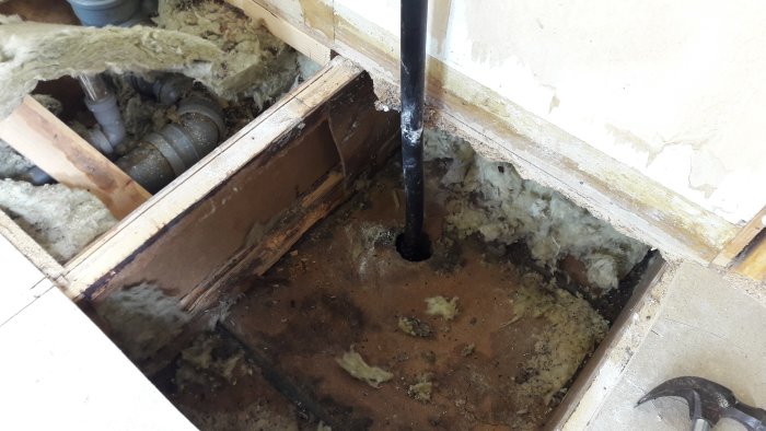 Öppnat golv i grovkök visar vattenledning, isolering och tecken på fukt och röta.