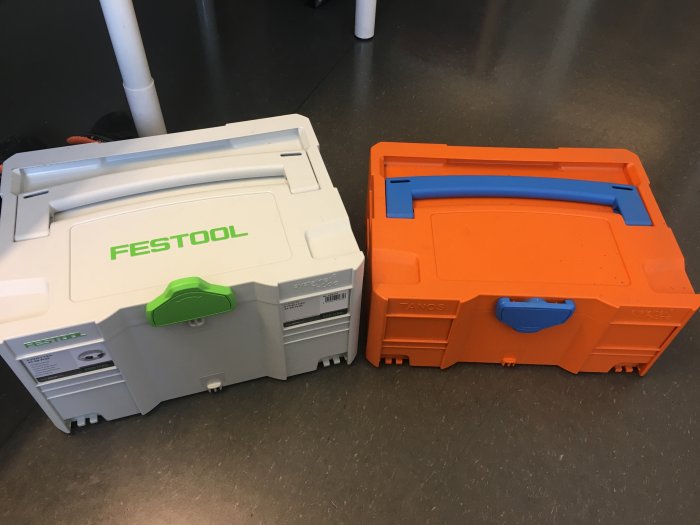 Två tomma verktygslådor, en vit med grön Festool-logotyp och en orange med blå detaljer.