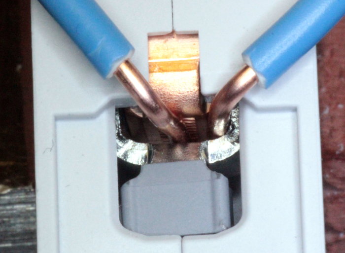 Två blå elektriska kablar kopplade i en Hager dvärgbrytare, en hårt och en löst fäst.