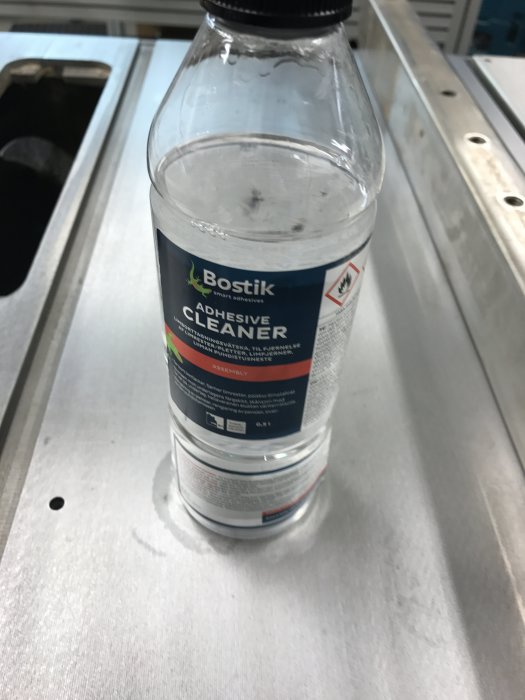 Flaska med etiketten 'Bostik Adhesive Cleaner' på en metallverkstadsbänk, använd för rengöring i renoveringsprojekt.