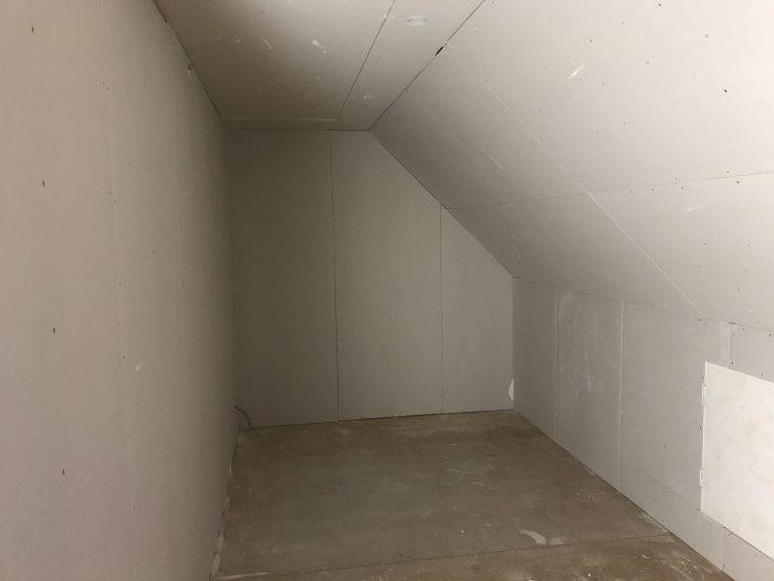 Oinredd övervåning med väggar klädda i nyinstallerade gipsplattor, förberedda för elinstallationer och takbelysning.