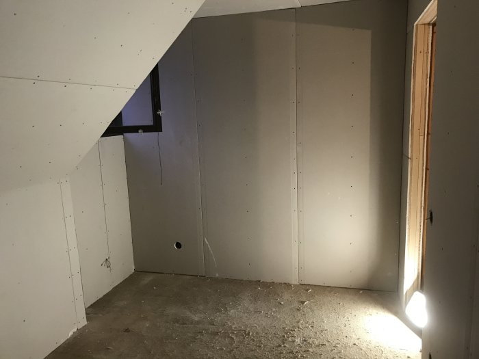 Oinredd övervåning under renovering med gipsskivor på väggarna och förberedelser för elinstallationer.