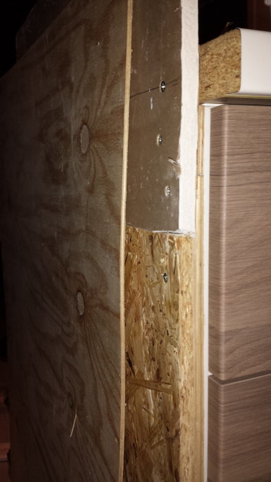Gipsskiva ovanpå OSB-skiva med en plywoodbit intill på en byggkonstruktion.