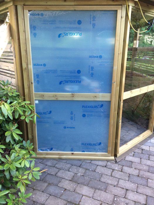 Dörrblad under konstruktion med träram och skyddsbelagt plexiglas i stående position utomhus.