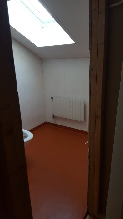 Utomhusrum med toalett och takfönster, oavslutade träbjälkar, vit kaklad vägg och orange golv.