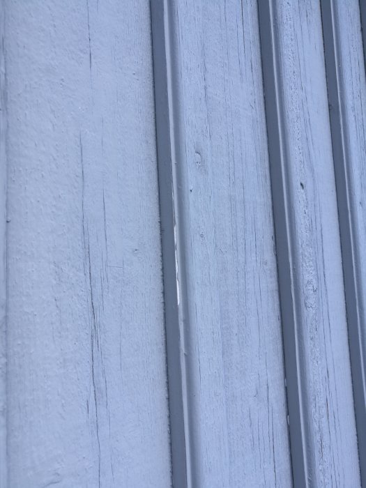 Närbild på fasad med vitmålad panel, slitage och sprickor syns, fråga om ommålning på forum.