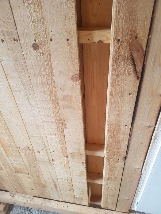 Öppnad väggstruktur med synliga reglar och plank för elinstallation.