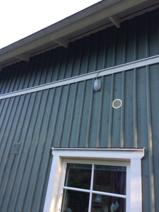 Ny utomhuslampa med rörelsesensor installerad på ett grönmålat hus med vita fönsterkarmar.