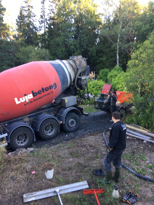 Betongbil häller ut betong i skottkärror på en byggplats med en person som övervakar.