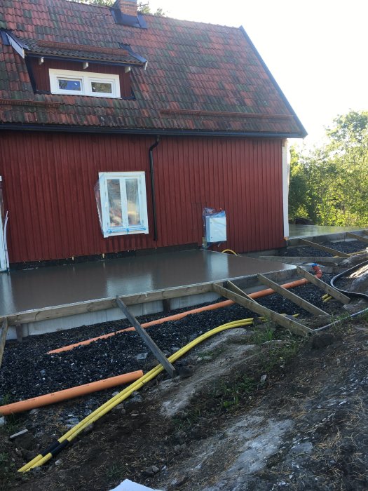 Nyguuten grund framför rött hus med formar och byggmaterial synliga.