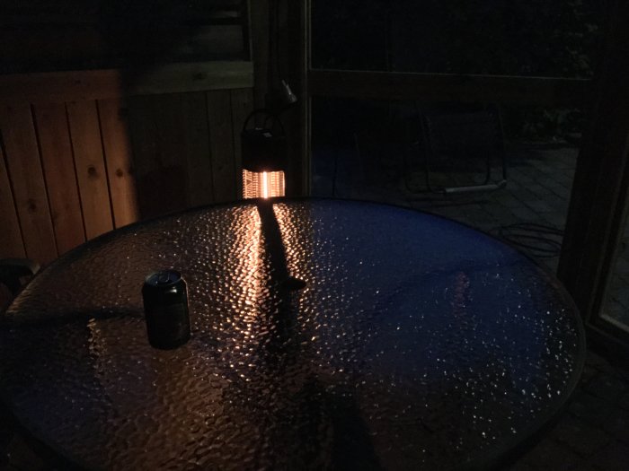 Reflexer från infravärme på ett glasbord utomhus i skymningen med en burk på bordet.