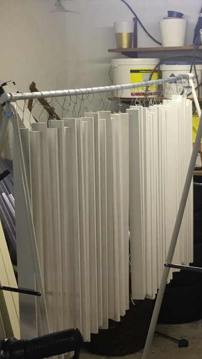 Nymålade vita spjälor hängande på tork på en modifierad klädställning med hemmagjorda najtrådshållare.