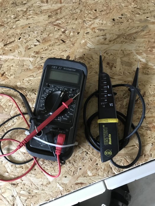 Digital multimeter och lysdiodpenna på spånskiva, verktyg för elektrisk felsökning.