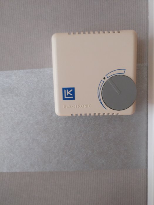 Äldre beige termostat på vägg med vred och LK Electronic-logotyp.