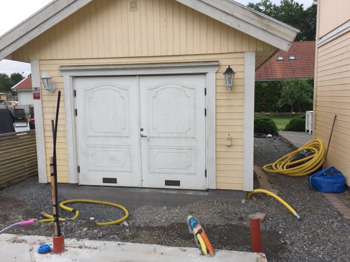 Byggarbetsplats med obehandlad dubbelgarageport, verktyg och slangar på en grusdriveway.