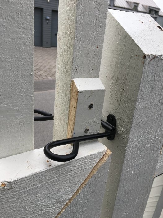 Närbild på en nyinstallerad svart grindkrok på en vit trägrind.