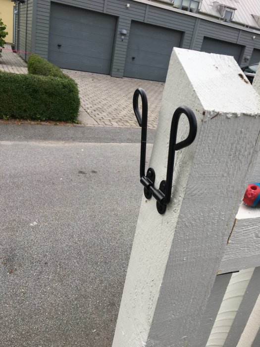 Nyinstallerade svarta smidesbeslag på vit grindstolpe framför garageuppfart.