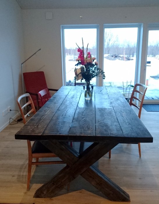 Hemgjort mörkt träköksbord med kryssben och infällda kapsylöppnare, vas med blommor på bordet.