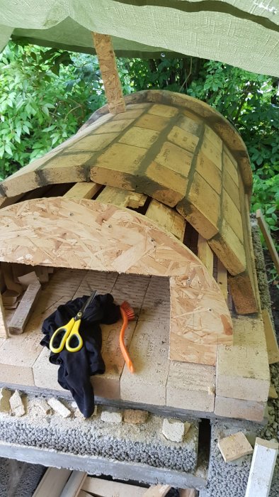 Byggfas av vedeldad ugn med isoleringsmaterial, tegelstenar och verktyg.