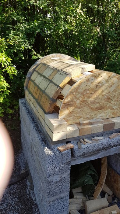 Delvis byggd vedeldad ugn av tegelsten med träform för valv under konstruktion.