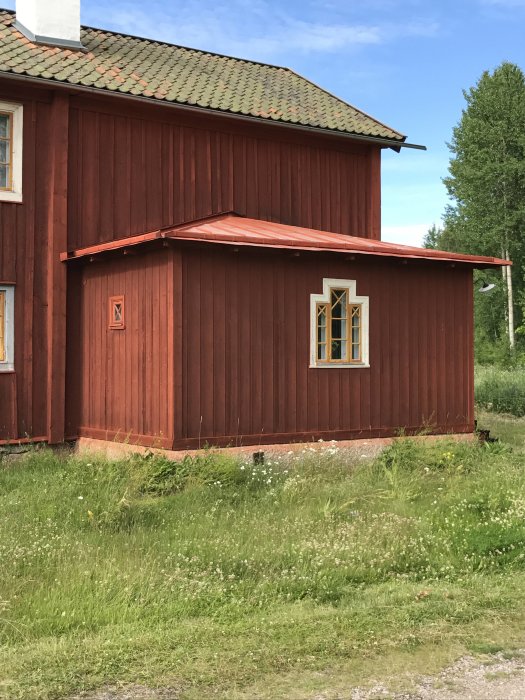 Rödmålat trähus med koppartak, omgivet av grönt gräs, i Gysinge byggnadsvårds stil.