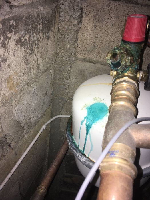 Vattenläckage med grön vätska på vit rörkoppling och vattenbehållare.