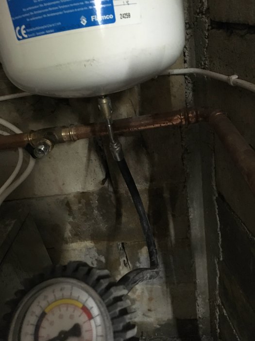 Expansionskärl och kopparledningar nära en vägg, med en manometer i förgrunden.