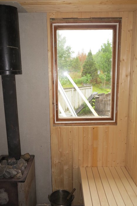 Interiör av bastu med vinkelplacerad övre bastulav bredvid fönster och kamin, underlav och fotstöd syns.