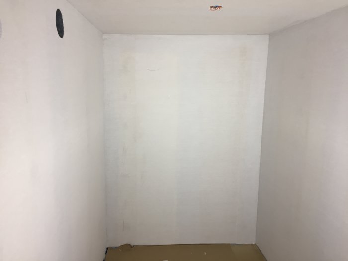 Hörn av ett rum med slipat spackel och uppsatt väv på väggarna samt microlit i taket.