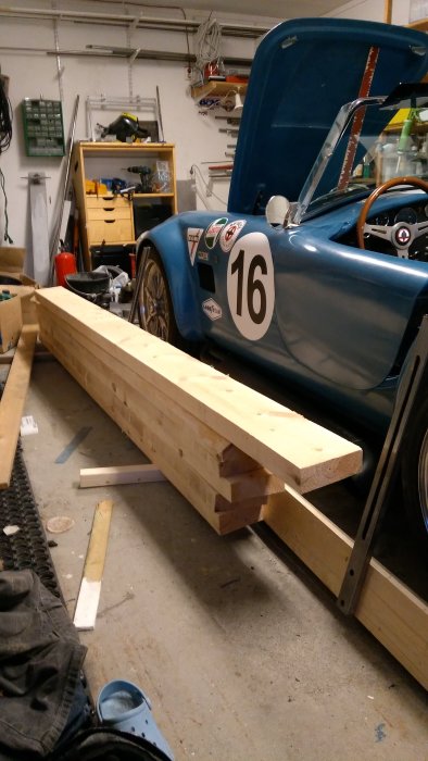 Nysågade träreglar bredvid en klassisk blå tävlingsbil i ett garage.