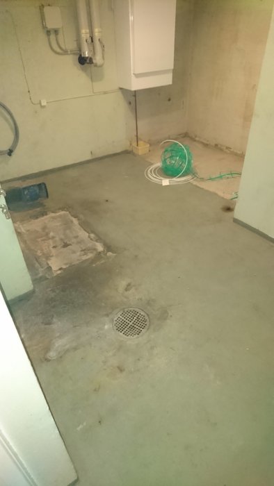 Tomt pannrum med avlägsnad oljepanna, synliga rör på väggen och ojämnt betonggolv med en avloppsbrunn.