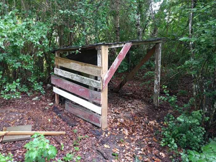 Nytt vedskjul av återvunnet material i skogsmiljö, byggt i ett fritidshusområde.