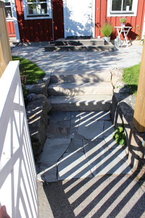 Nygräddat gräs vid en husentré med återanvända granitstolpar och sandstensgång med stentrappor.