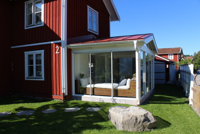 Rödmålat hus med inglasad veranda, nygräst tomt, granitsten och sandstensplattor framför huset.