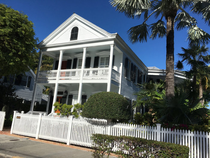 Vit trävilla med verandor och staket i Key West, soligt väder, palmer och klarblå himmel.